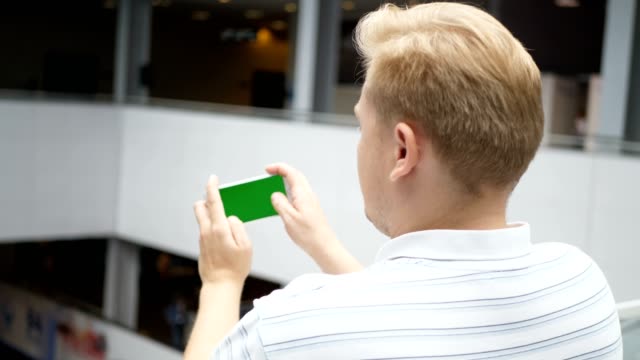 Young-teenager-playing-game-on-smartphone-in-cafe.-Young-happy-man-playing-games-on-smartphone.-Smartphone-turns-on-on-white-background.-Easy-customizable-green-screen.-Computer-generated-image.