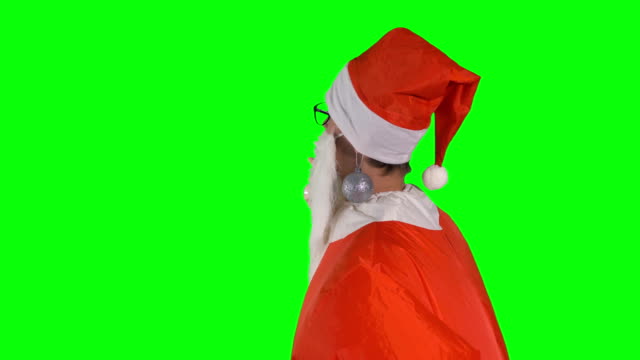 Santa-Claus-mit-Christbaumkugeln-an-seinem-Ohr-weist-auf-ein-unsichtbares-Objekt.