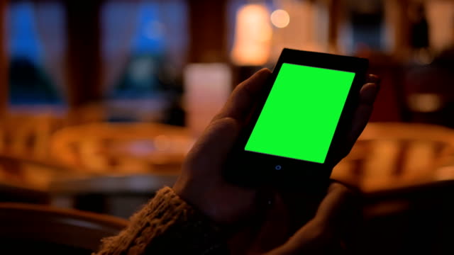 Woman-looking-at-smart-phone-phone-with-green-screen-in-cafe