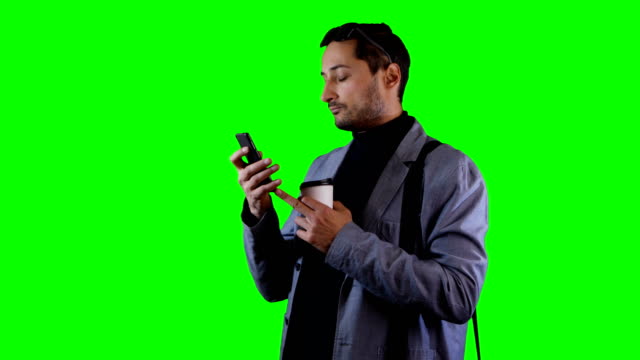 Man-in-suit-and-black-sunglasses-use-mobile-and-hold-coffee-cup.-Green-screen,-footage.