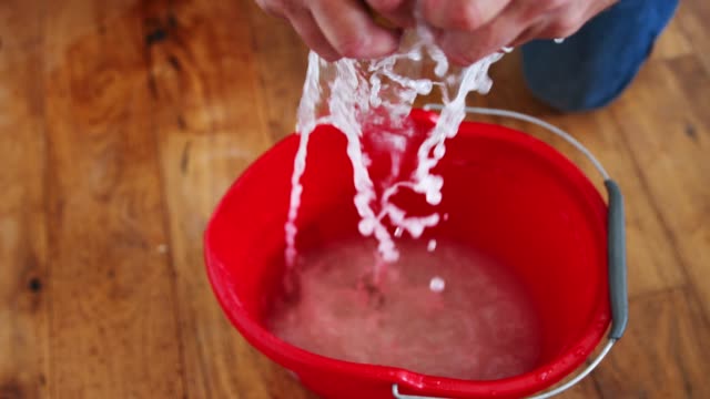 Close-Up-Of-Man-Squeezing-Water-Into-Bucket-After-Domestic-Leak