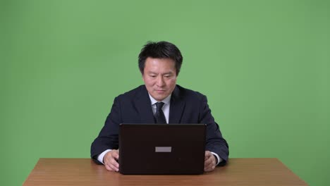 Mature-Japanese-businessman-against-green-background