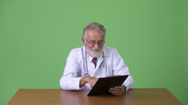 Hübscher-senior-bärtigen-Mann-Arzt-vor-grünem-Hintergrund