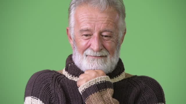 Handsome-senior-bearded-man-wearing-warm-clothing-against-green-background