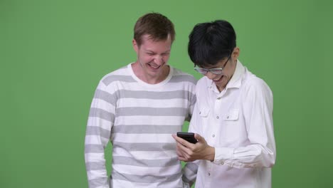 Zwei-glückliche-multiethnischen-Jungunternehmer-mit-Handy-zusammen