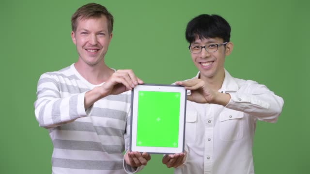Jóvenes-empresarios-multiétnicos-de-dos-felices-mostrando-tableta-digital-de-la-cámara-juntos