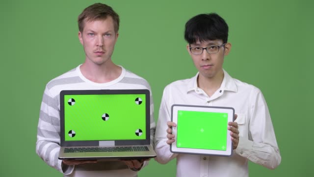 Dos-jóvenes-empresarios-multiétnicos-que-muestra-el-ordenador-portátil-y-tableta-digital-de-la-cámara