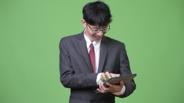 Young-happy-Asian-businessman-smiling-while-using-digital-tablet