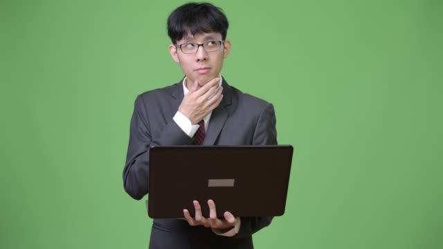 Young-Asian-businessman-thinking-while-using-laptop