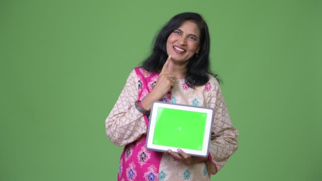 Reife-glücklich-schöne-indische-Frau-denken-und-zeigt-digital-Tablette
