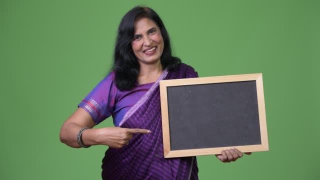 Mature-happy-beautiful-Indian-woman-pointing-to-blackboard