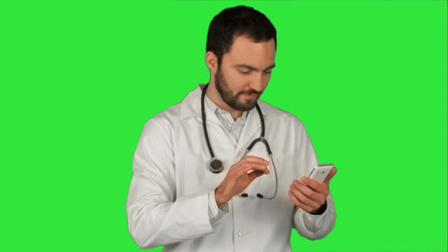 Medizinische-männlichen-Arzt-senden-eine-Nachricht-mit-seinem-cellphone,-lächelnd-und-stehen-auf-einem-grünen-Bildschirm-Chroma-Key