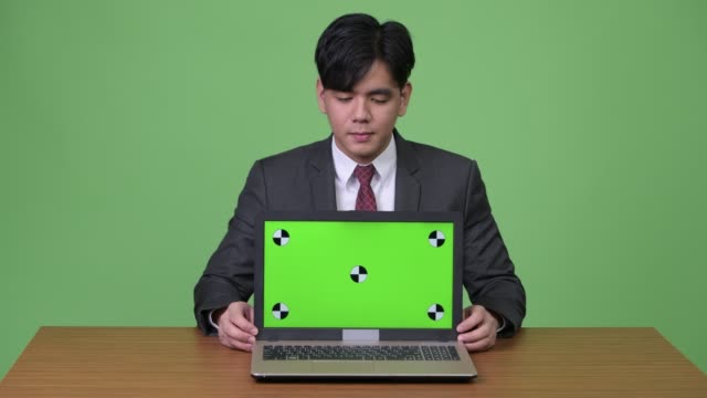 Schöne-asiatische-Jungunternehmer-zeigen-Laptop-vor-grünem-Hintergrund