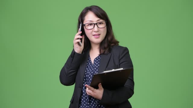 Madura-empresaria-asiática-hermosa-usando-teléfono-manteniendo-portapapeles