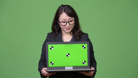 Madura-empresaria-asiática-hermosa-mostrando-portátil-sobre-fondo-verde