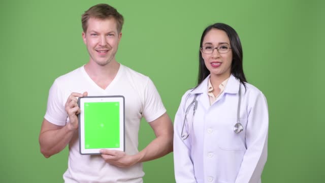 Young-Asian-woman-doctor-with-young-man-patient-showing-digital-tablet