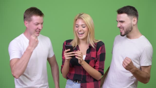 Three-happy-young-friends-using-phone-together-and-getting-good-news