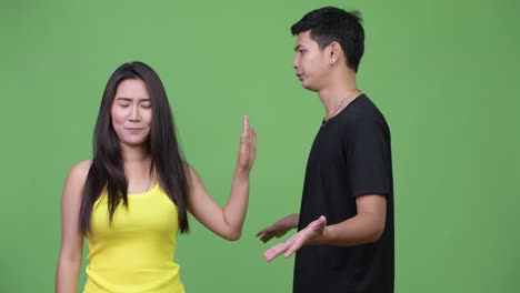 Young-Asian-woman-showing-stop-gesture-to-young-angry-Asian-man