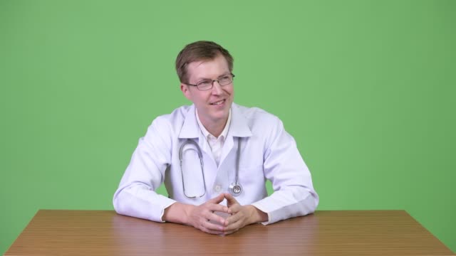 Portrait-Of-Young-Happy-Man-Doctor-Sitting-And-Thinking