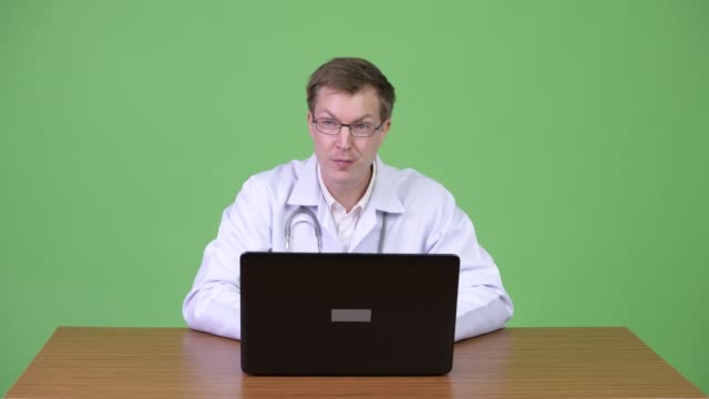 Médico-hombre-sentado-y-usando-la-computadora-portátil-mientras-habla-y-saludo-paciente