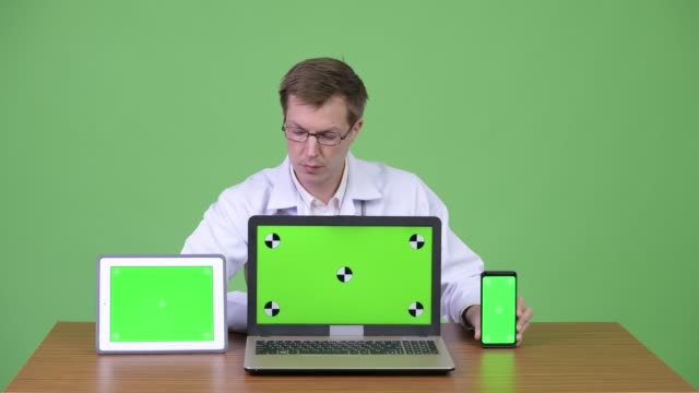 Médico-sentado-y-mostrando-la-clave-pantalla-verde-del-croma-portátil-Tablet-computadora-Digital-y-teléfono-móvil