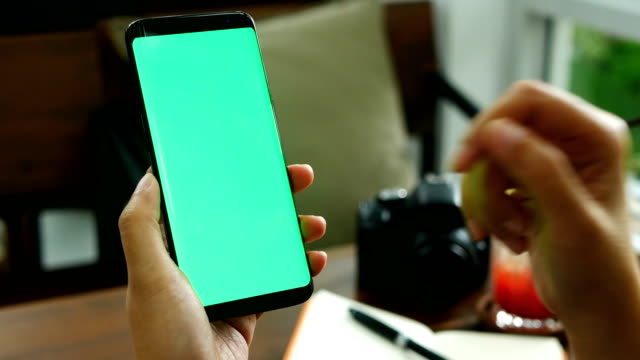 4K-footage.-close-up-woman-hand-holding-smart--hone-with-green-screen-at-coffee-shop,-slide-finger-on-phone-screen-for-reading-content-on-mobile