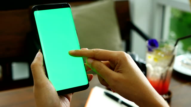 4K-footage.-close-up-woman-hand-holding-smart-phone-with-green-screen-at-coffee-shop,-using-finger-touch-on-phone-screen