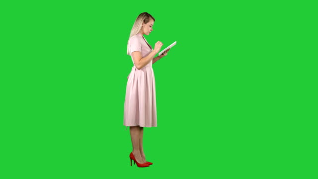Mujer-joven-en-vestido-rosa-vista-uso-de-tableta-a-una-pantalla-verde-Chroma-Key