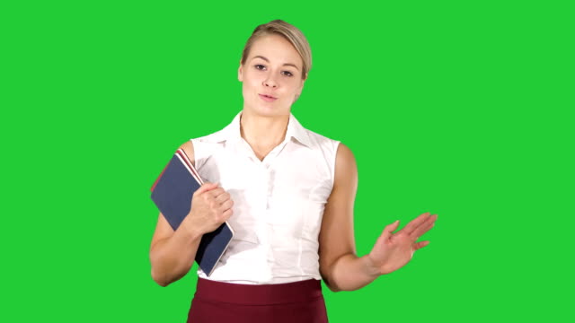 Beautiful-teacher-with-notebooks-explaining-something-to-camera-on-a-Green-Screen,-Chroma-Key
