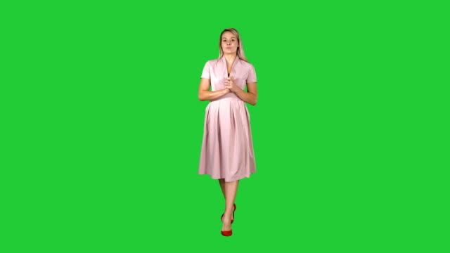 Happy-young-woman-inpink-dress-is-walking-towards-camera-and-talking-on-a-Green-Screen,-Chroma-Key