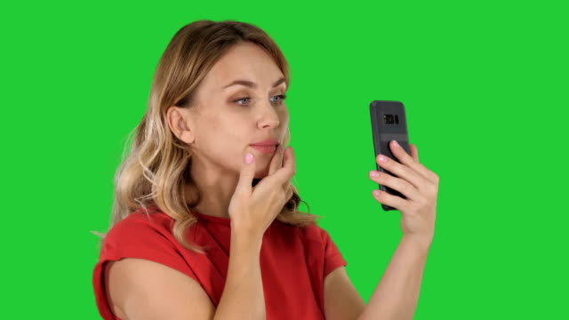 Schöne-Frau-putzen-mit-ihrem-Telefon-wie-ein-Spiegel-auf-einem-Green-Screen,-Chroma-Key