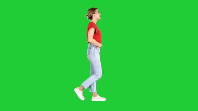 Fit-girl-holding-her-hands-in-the-pockets-of-blue-jeans-walking-on-a-Green-Screen,-Chroma-Key