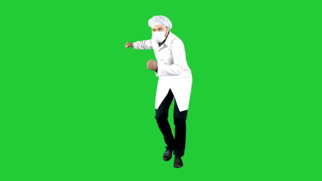 Doctor-wearing-his-uniform-and-wearing-a-mask-he-is-walking-in-a-funny-way-on-a-Green-Screen,-Chroma-Key