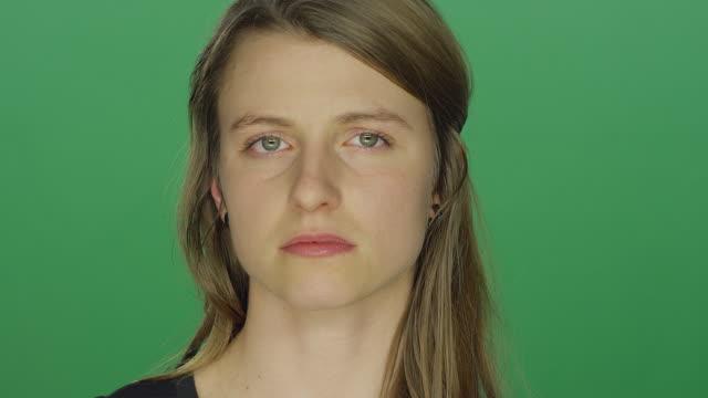 Young-women-looks-sad-and-cries-and-wipes-away-a-tear,-on-a-green-screen-studio-background