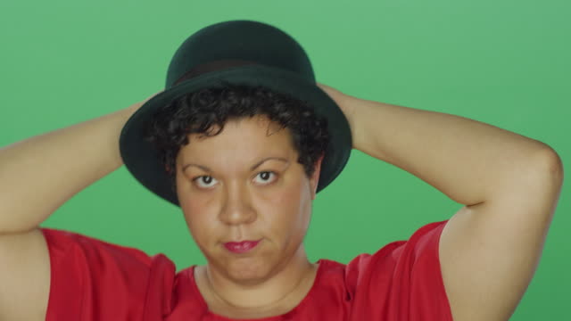 Woman-wearing-a-hat-smiles-and-dances,-on-a-green-screen-studio-background