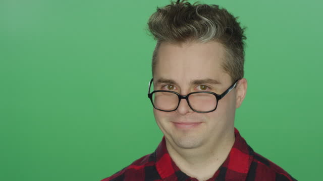 Young-man-with-glasses-staring-ahead,-on-a-green-screen-studio-background