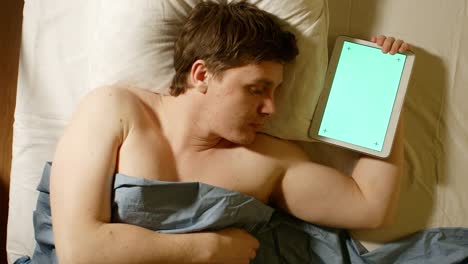Kaukasischer-junge-Mann-schläft-und-hält-einen-Tablet-PC-in-der-Hand-(Greenscreen)