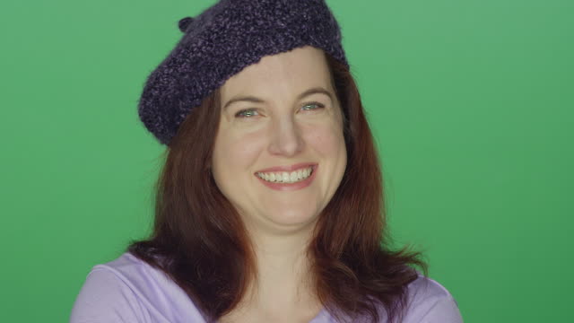 Young-redhead-woman-wearing-a-beret-laughing-and-smiling,-on-a-green-screen-studio-background