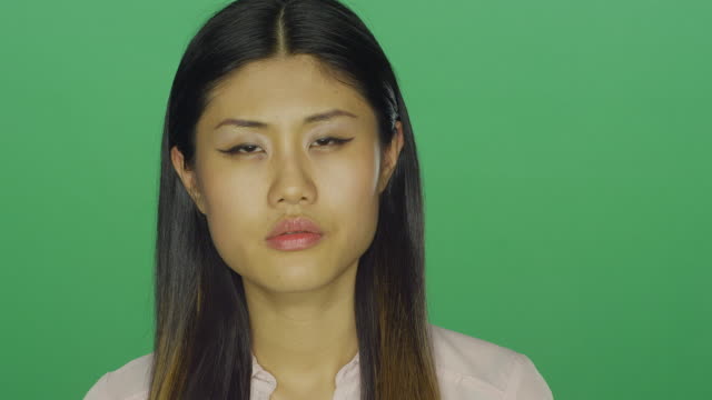Beautiful-Asian-woman-stares-ahead-and-then-smiles,-on-a-green-screen-studio-background