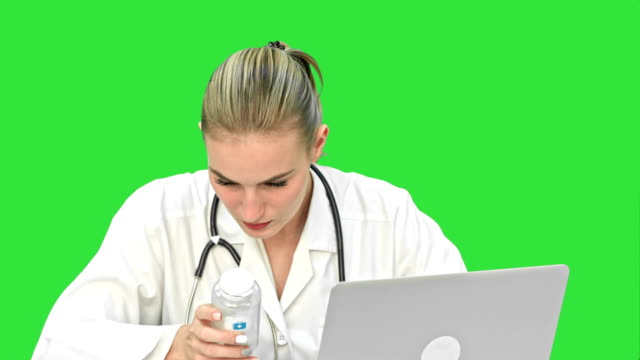 Young-female-doctor-typing-on-laptop,-trying-to-find-a-manual-of-pills-in-the-Internet-on-a-Green-Screen,-Chroma-Key