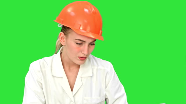 Stressed-female-engineer-in-helmet-checking-constraction-plan-on-a-Green-Screen,-Chroma-Key
