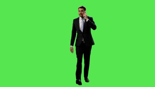 Businessman-in-a-suit-is-walking-and-talking-on-mobile-phone-on-a-mock-up-green-screen-in-the-background.
