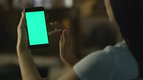 Chica-adolescente-está-utilizando-Smartphone-con-la-pantalla-verde-en-el-modo-de-retrato-en-la-noche.-Estilo-de-vida-casual.