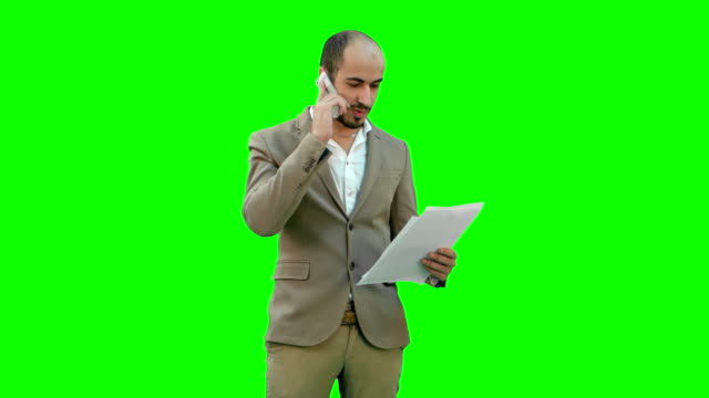 Junger-Mann-im-Anzug-am-Telefon-sprechen-und-halten-Papiere-auf-einem-Green-Screen,-Chroma-Key