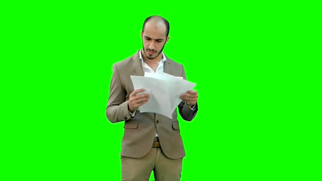 Serious-young-businessman-standing-and-reading-some-documents-on-a-Green-Screen,-Chroma-Key