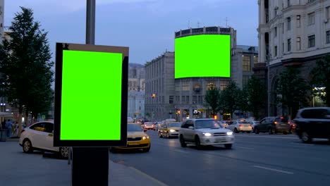 Two-billboards-with-a-green-screen.-In-the-evening,-on-a-busy-street.