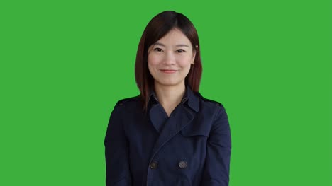 Junge-asiatische-Frau-trägt-einen-blauen-Mantel.-Verwendung-von-Smartphone,-Digital-Tablette-und-Blick-in-die-Kamera.-Frau-stand-vor-einem-Greenscreen-für-Chroma-Key.