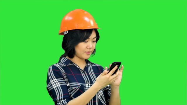 Architektin-mit-orange-Helm-mit-Smartphone-auf-einem-Green-Screen,-Chroma-Key