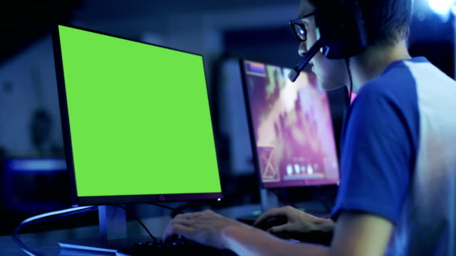 Professional-Boy-Gamer-Plays-in-Video-Game-on--Green-Screen-Display.-He-Plays-on-a-eSports-Tournament/-in-Internet-Cafe.-He-Wears--Headset-and-Speaks-Commands-into-Microphone.
