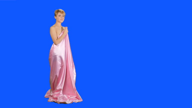 Beautiful-girl-in-pink-satin-bedsheet-poses-for-camera-at-blue-background